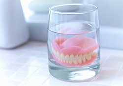 Dentures in a glass of clear fluid on white tiled countertop