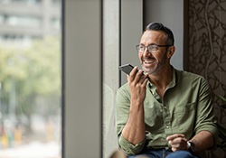 Man smiling while talking on speaker phone