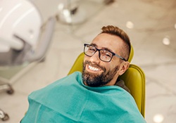 Man with glasses smiling while sitting in treatment chair