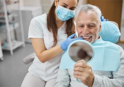 An older man admiring his new dental implants in a hand mirror