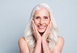 A closeup of a smiling gray-haired lady holding her cheeks