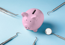A pink piggy bank surrounded by dental tools on a blue background