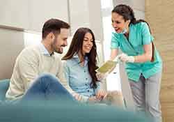 Smiling couple reviewing pamphlet with dental assistant